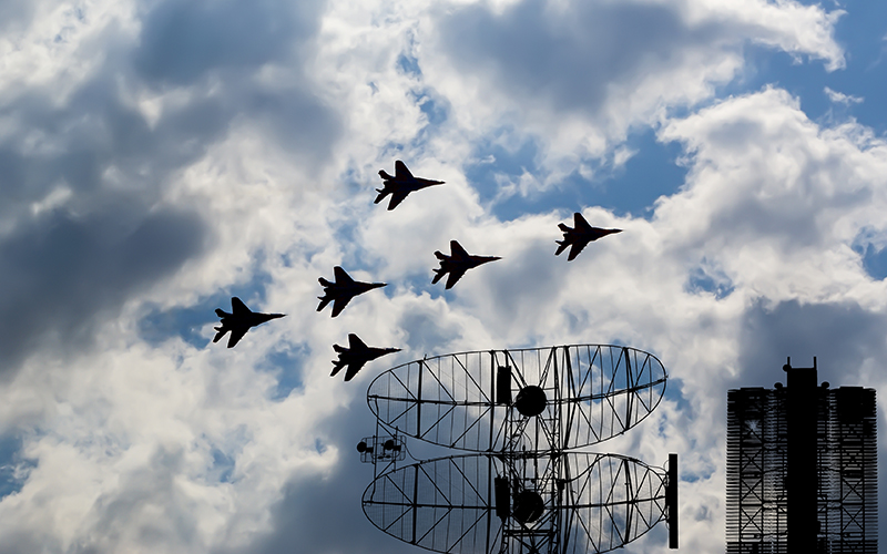 four jets flying over a radar dish